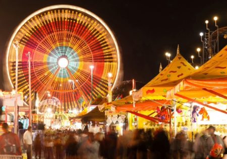 Night time view of a carnival with the Ferris Wheel against the sky